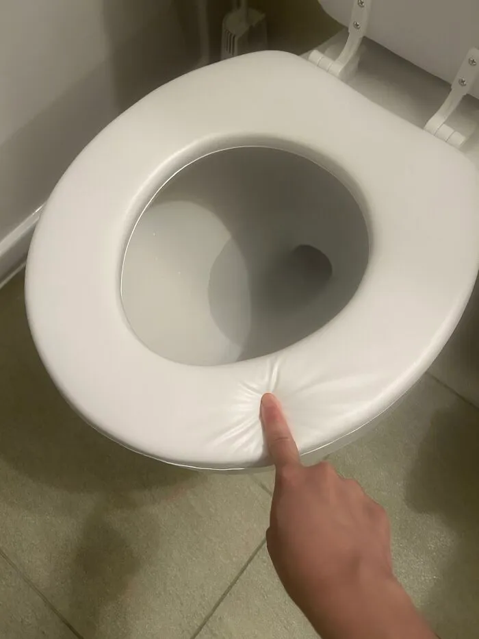 A finger pressing down on a soft, squishy toilet seat in a house with strange design decisions.