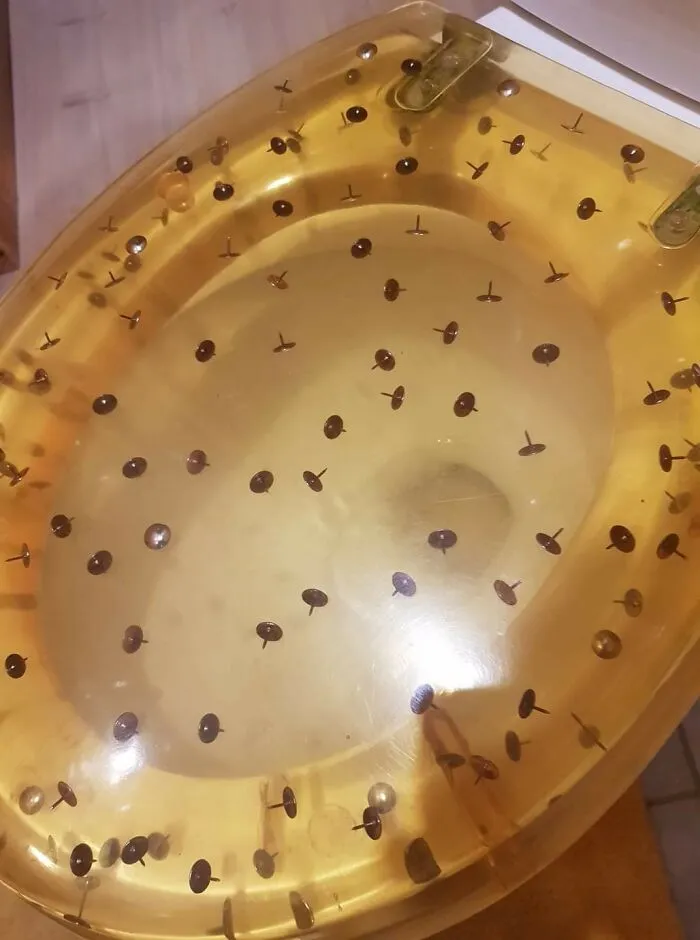A clear yellow toilet seat containing embedded metal thumbtacks in a house with poor design vision.
