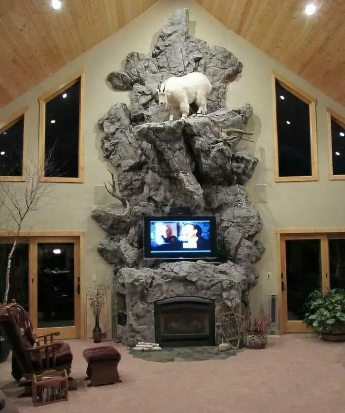 A massive faux-rock fireplace wall with a taxidermy goat in a custom house design