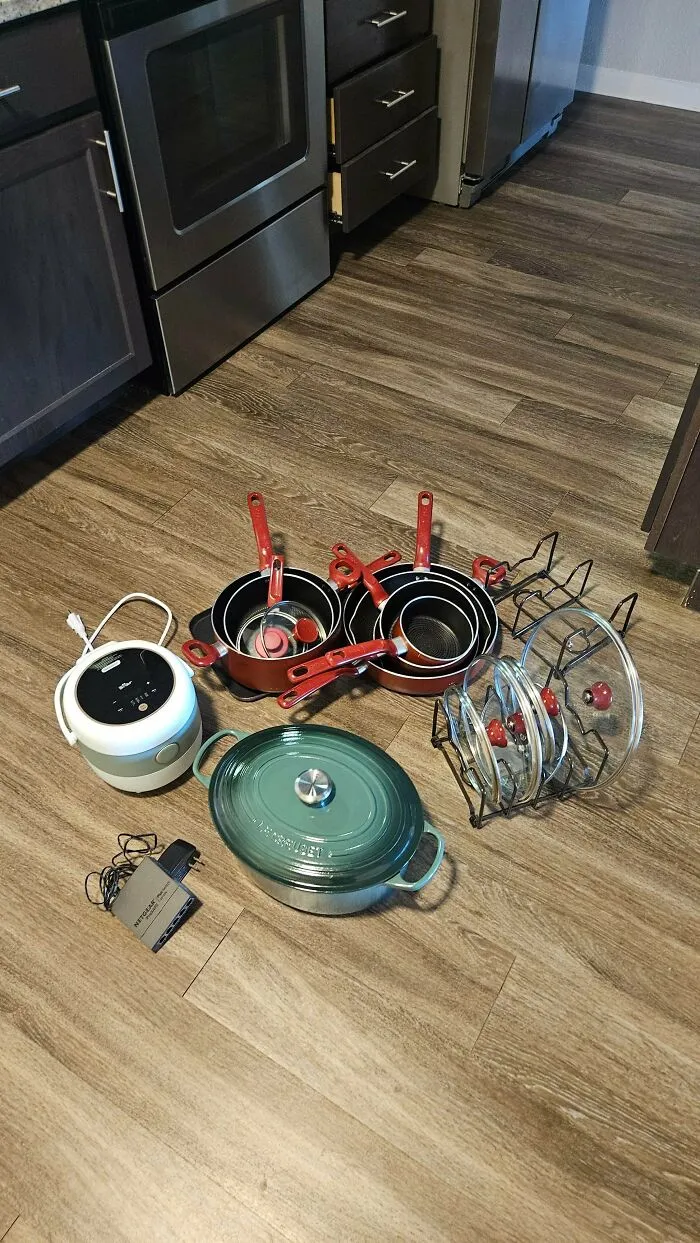 Dumpster diving kitchen finds including pots, pans, lids, and kitchen appliances on wooden floor