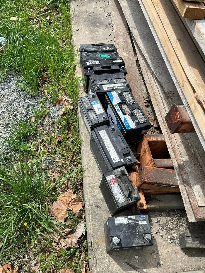 Used car batteries collected from dumpster diving lined up on a sidewalk near grass
