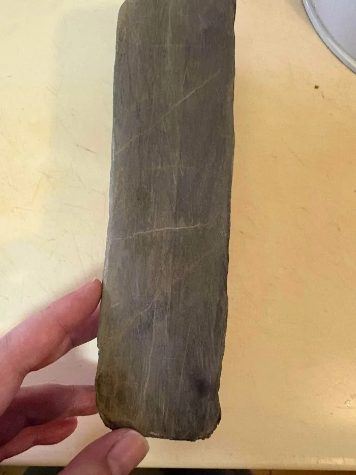 A hand holding a worn stone sharpening block, showing old products that continue to serve their purpose.