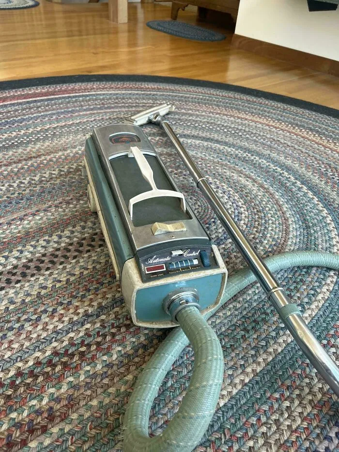Vintage canister vacuum cleaner on a braided rug, showcasing durable old products.