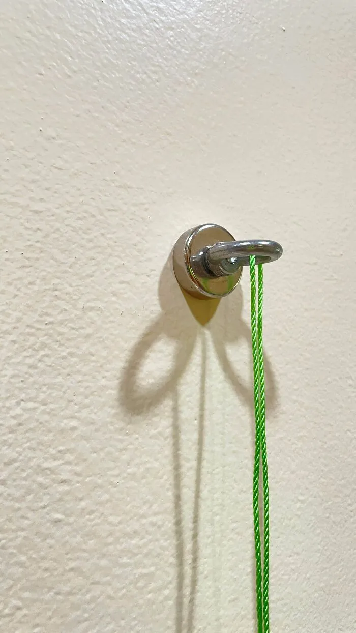 A sturdy metal eyelet magnet with a green cord mounted on a wall demonstrating long-lasting old products.
