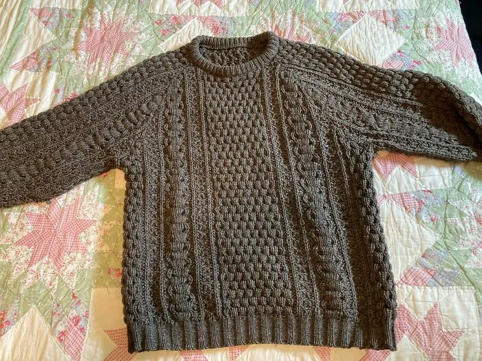 Thick knitted brown wool sweater laid on a patterned quilt, one of many old products still in use.