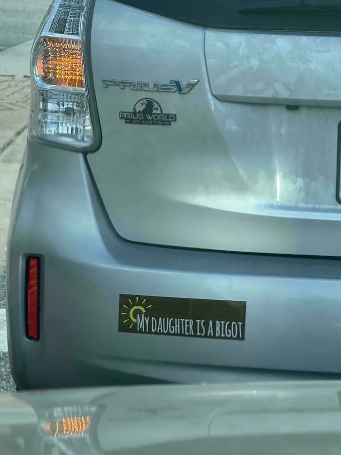A funny bumper sticker on a silver Prius reading MY DAUGHTER IS A BIGOT.