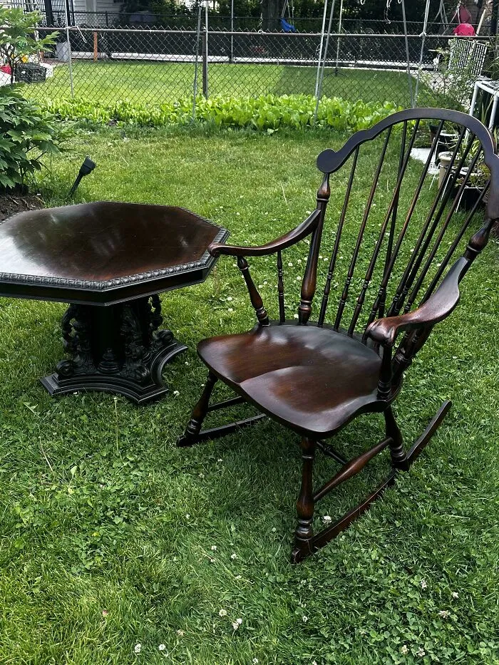 A classic dark wood rocking chair and matching side table placed on a lawn, representing old treasures.