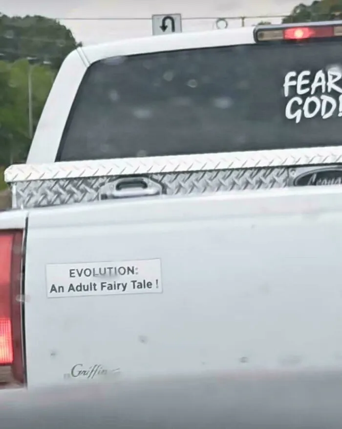 Controversial bumper stickers on a white truck reading EVOLUTION: An Adult Fairy Tale!