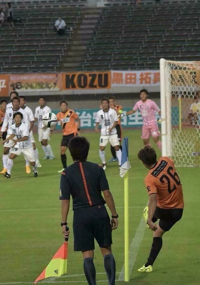 Soccer player kicks ball near corner flag while referee and players watch, creating an optical illusion