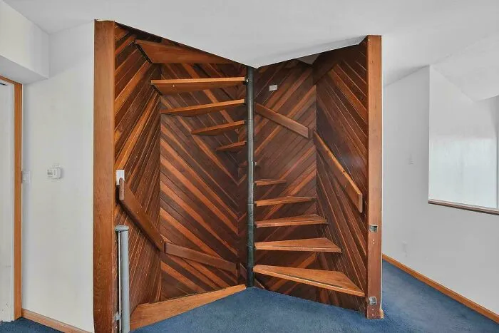 Wooden spiral staircase blending into paneled wall in an indoor setting