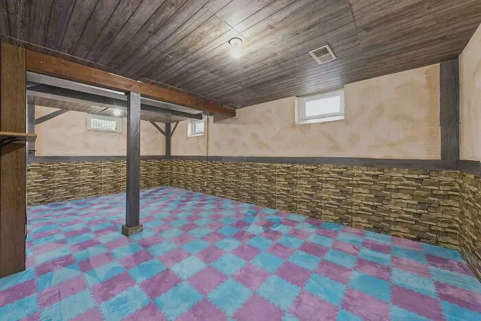 Empty basement room with colorful checkered carpet and stone-themed wall design
