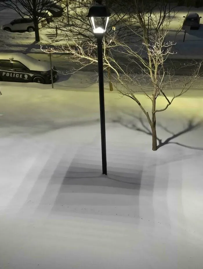 Snow shadows create optical illusion around a streetlamp at night confusing the eye