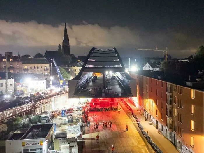 Large bridge structure suspended over street at night creating an unusual optical illusion