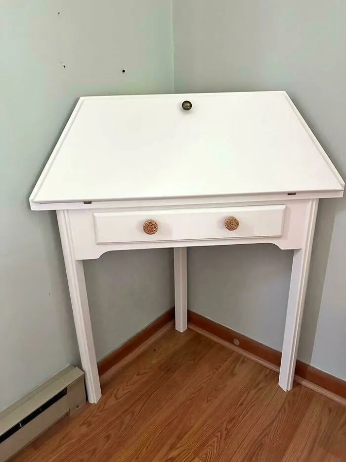 White desk with drawers appears to stand on three legs and a wall corner, confusing the eye