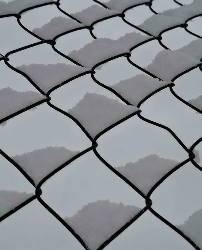 Snow settling in diamond shapes on chain-link fence confusing the eye