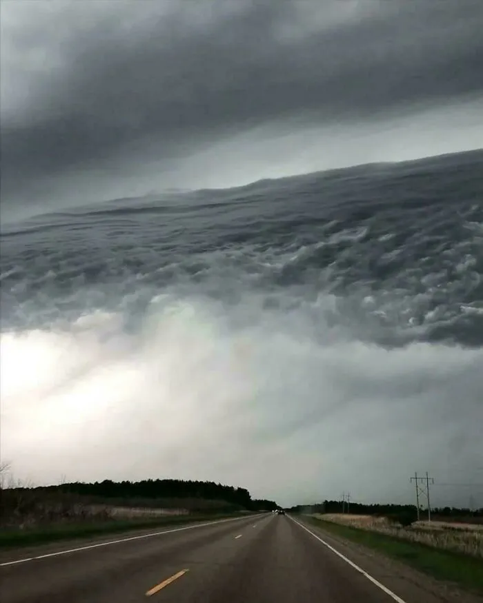 Road under a sky with clouds forming an optical illusion resembling a turbulent sea