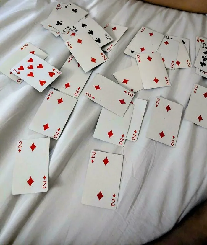 A pile of playing cards with mostly number twos facing up on white bedsheets