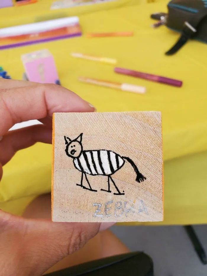 A hand holding a wooden block with a funny zebra child drawing, showing unhinged things wives do