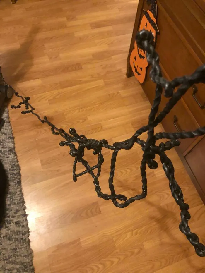 A twisted black metal stand standing on a wooden floor, illustrating unhinged things wives do.