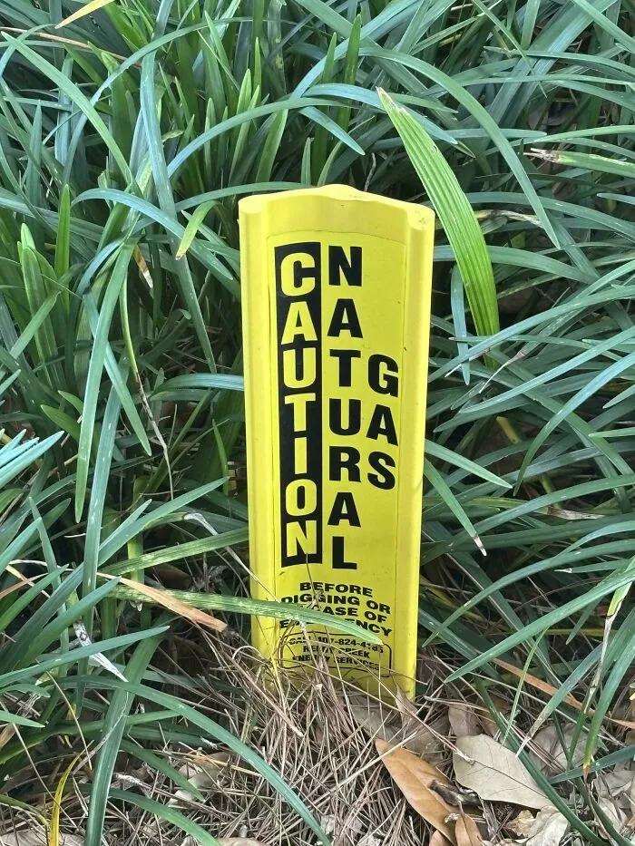 Yellow natural gas caution marker with scrambled vertical text, an instance of hilarious badly designed signs.