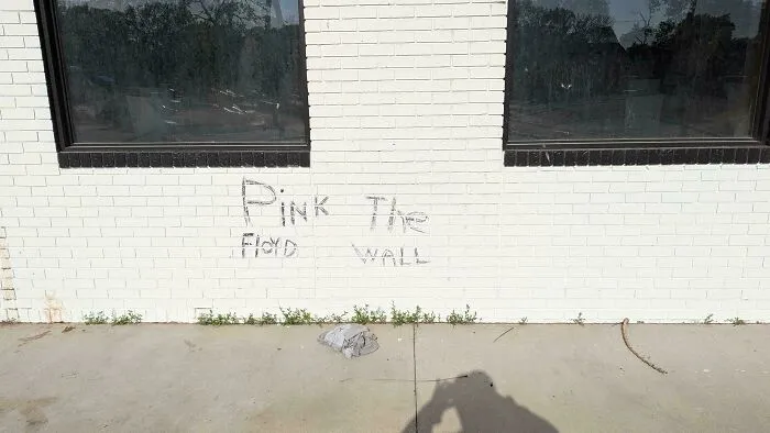 Graffiti on a white brick wall reading Pink The Floyd Wall, an example of a badly designed sign.
