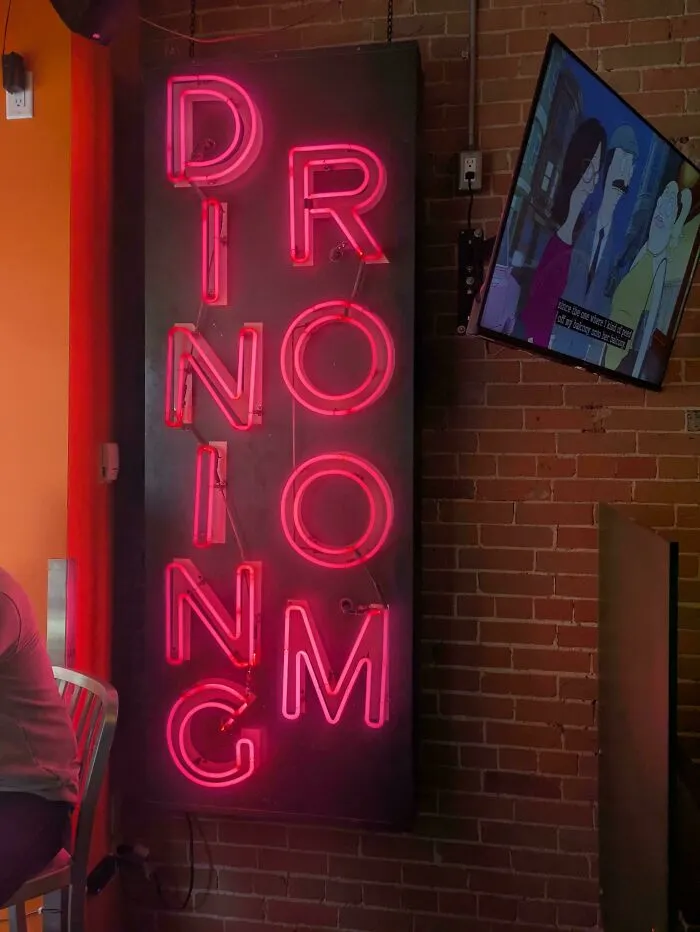 A glowing pink neon sign spelling Dining Room in a confusing vertical layout, an example of badly designed signs.
