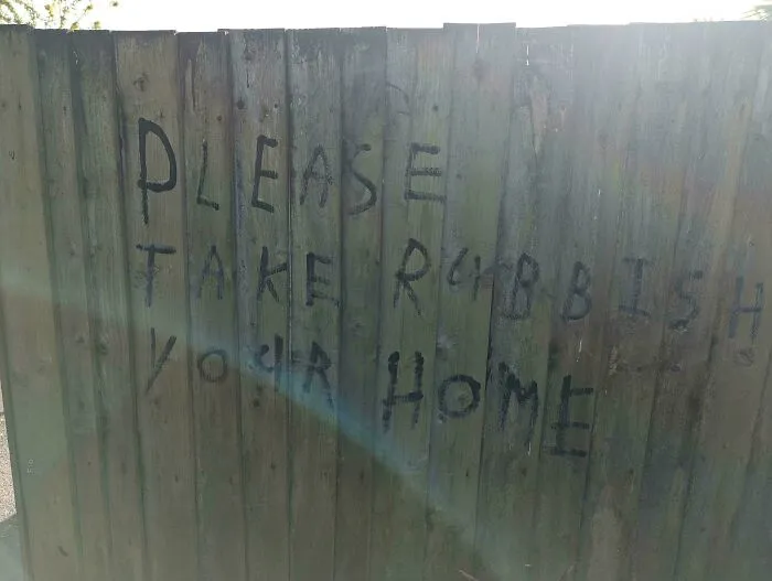 Graffiti on a wooden fence with misplaced words creating a badly designed sign.