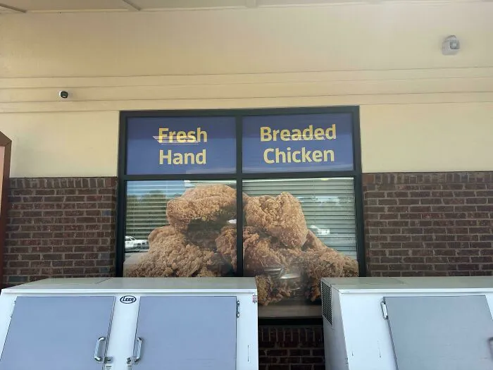 A restaurant store front featuring a badly designed sign that reads Fresh Hand Breaded Chicken