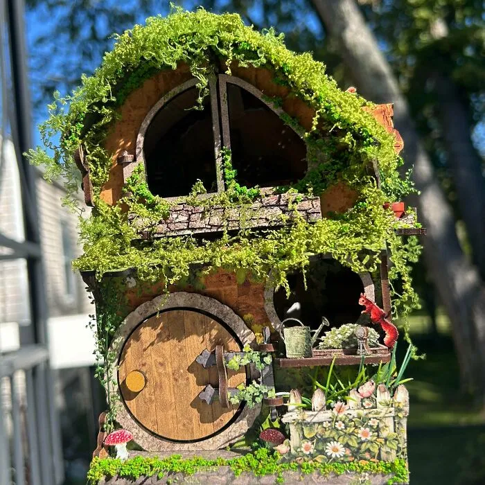 A whimsical mossy hobbit hole book nook with a round wooden door