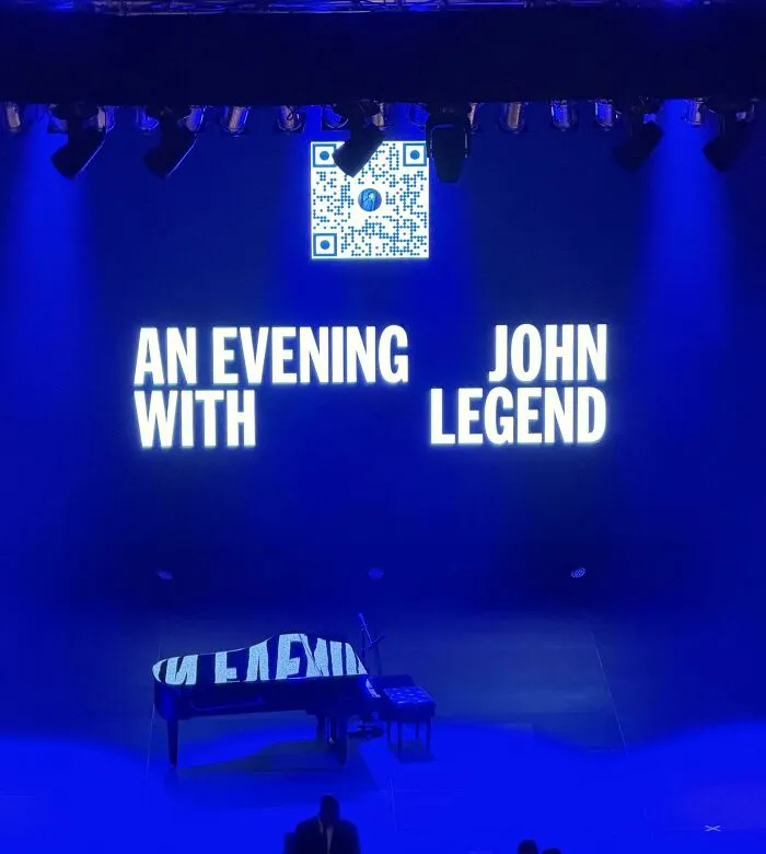 Concert stage screen displaying poorly arranged text in a funny, hilarious badly designed sign layout.
