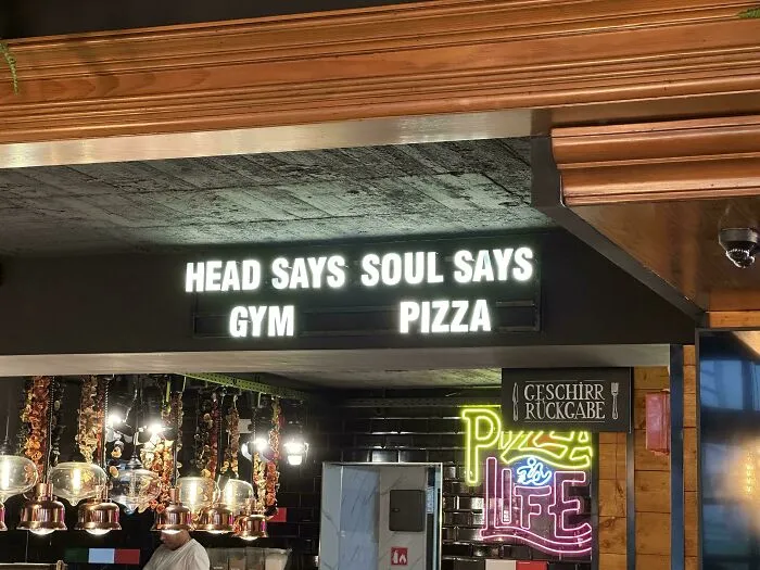An illuminated restaurant sign featuring badly designed signs stating HEAD SAYS GYM SOUL SAYS PIZZA.