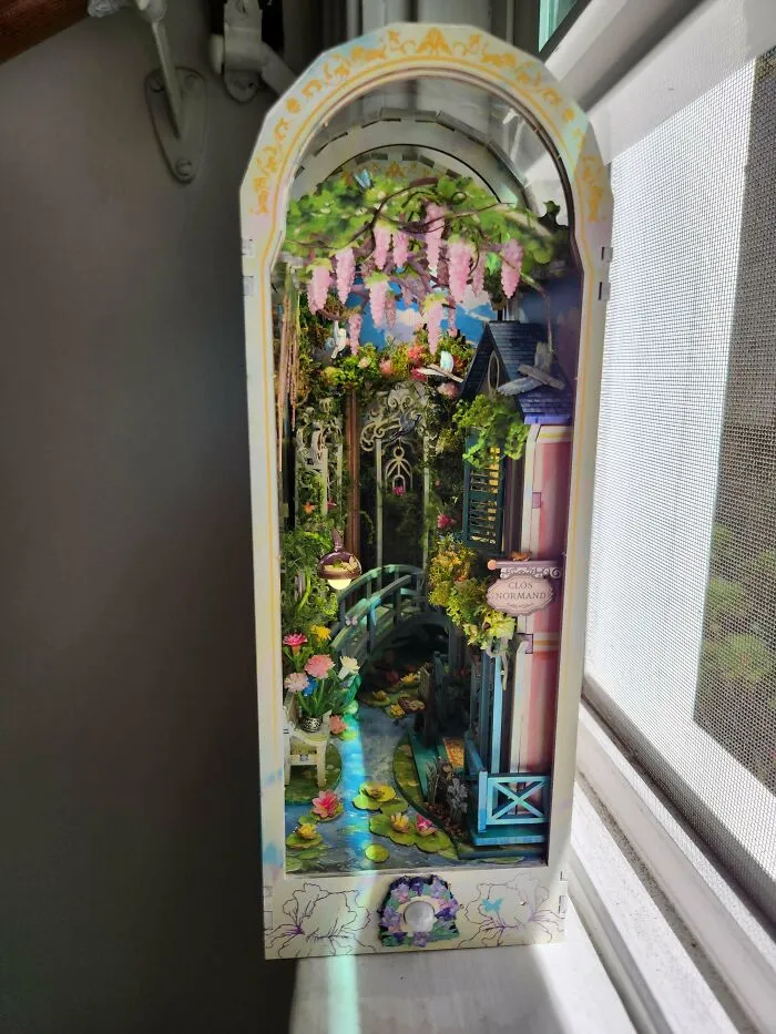 A magical garden path book nook with a bridge and hanging flowers on a windowsill