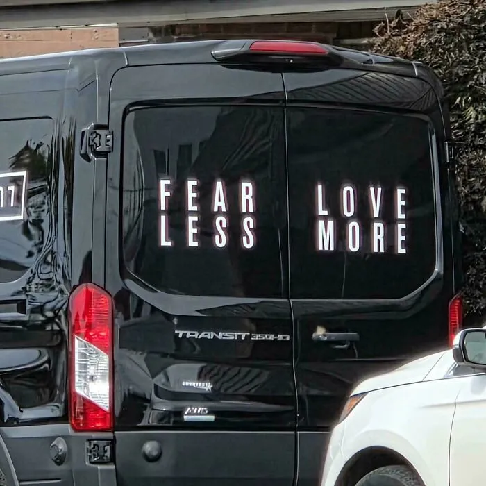 Black van doors showing badly designed signs split in half, reading FEAR LESS LOVE MORE in a confusing layout.