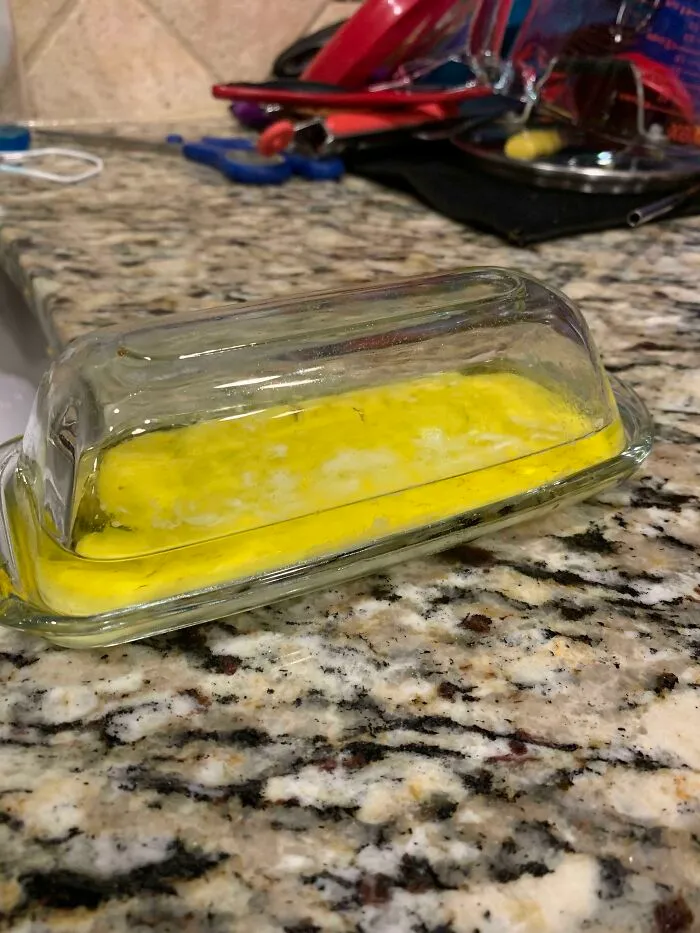 A stick of butter melted in a glass dish on a counter, showing funny things wives do