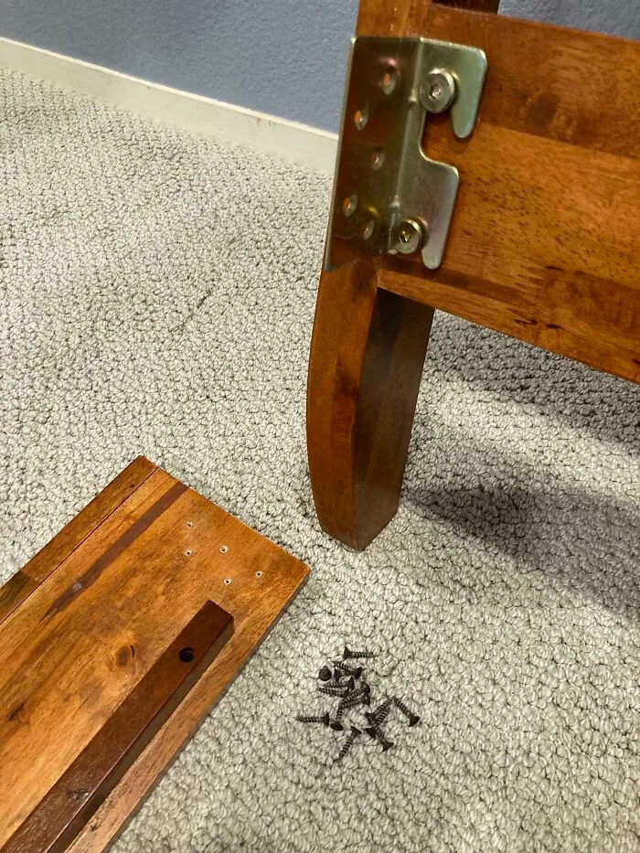 Unassembled wooden furniture parts and screws on carpet, showing funny things wives do