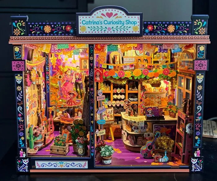 A colorful Day of the Dead themed book nook with miniature skeleton figurines and vibrant decorations.