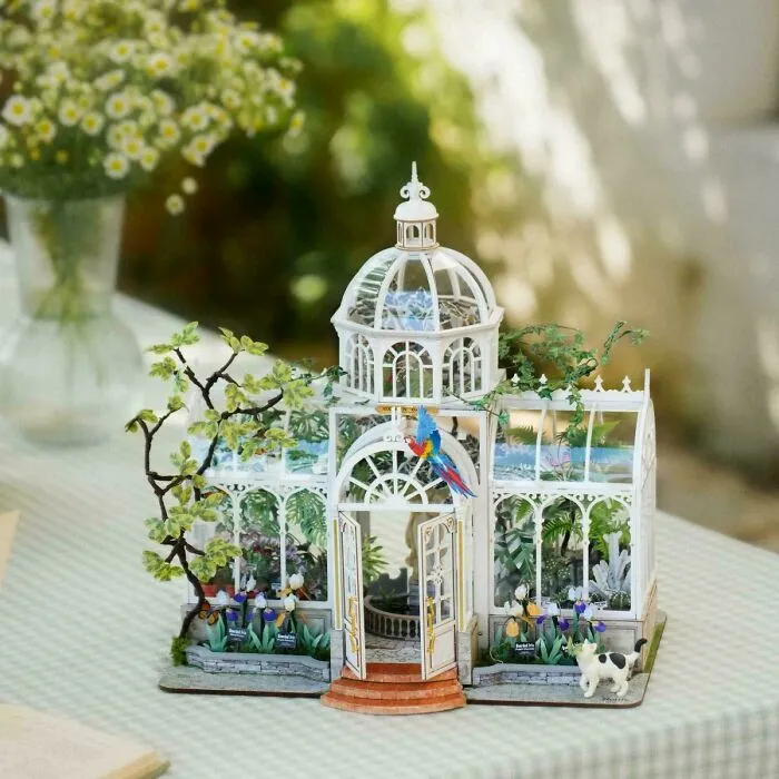 A delicate white conservatory greenhouse miniature kit with paper plants and a small parrot.