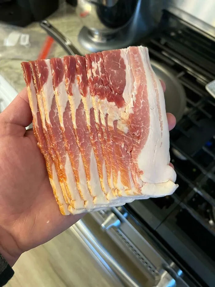 A hand holding a block of uncut bacon, illustrating funny things wives do