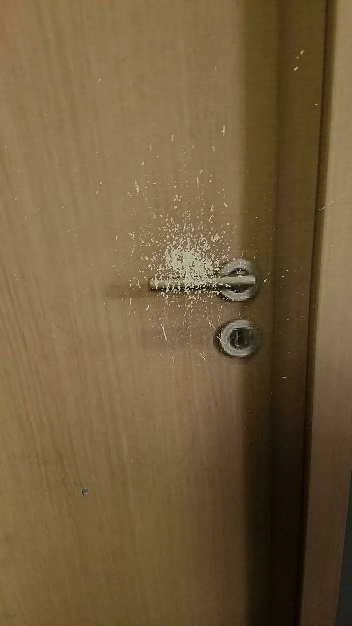 Wooden door handle with worn paint splatter showing how time slowly reshapes frequently touched surfaces.
