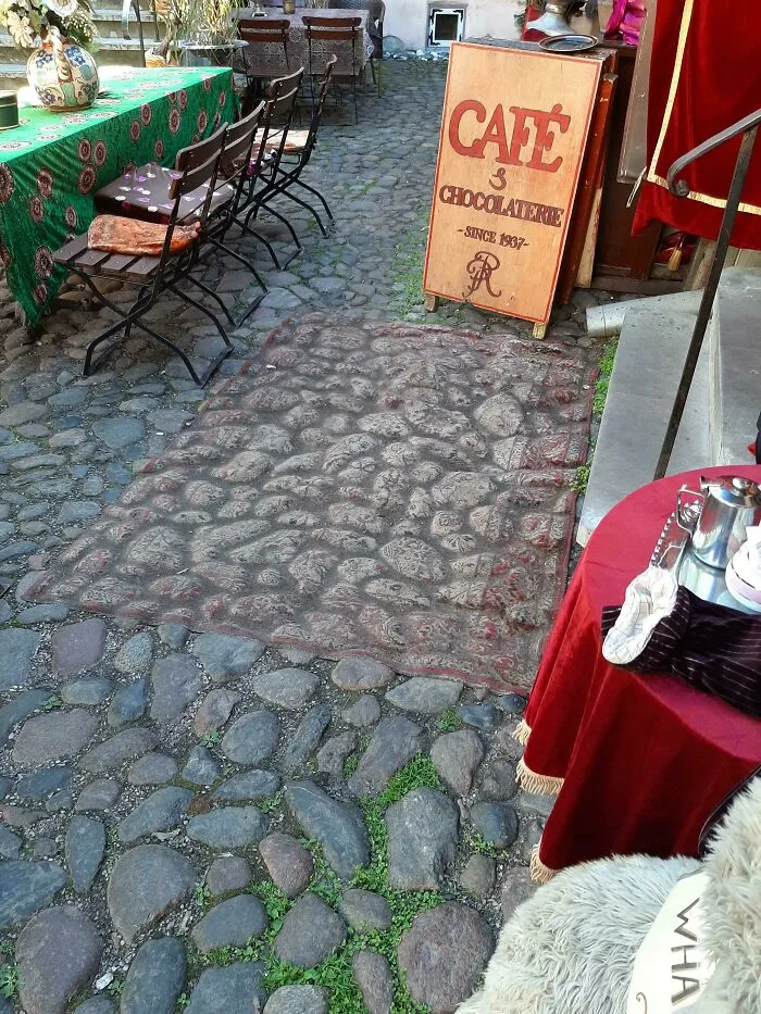 Outdoor cafe setting with a patterned rug on cobblestone showing how time slowly reshapes outdoor spaces.