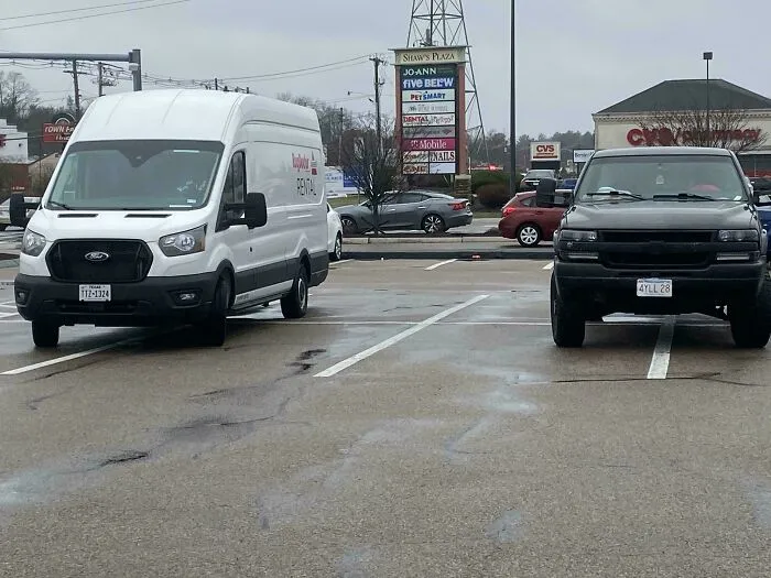 A white rental van and a black truck parked badly, showcasing how entitled people take up multiple spaces.