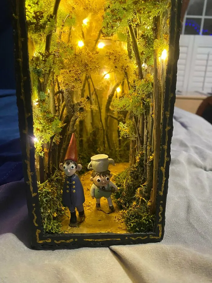 An whimsical book nook showing miniature characters walking through a glowing autumn forest