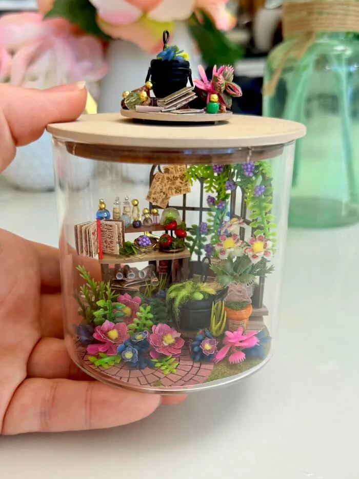 A whimsical wizard laboratory miniature inside a jar, featuring colorful flowers, tiny potion bottles, and books.