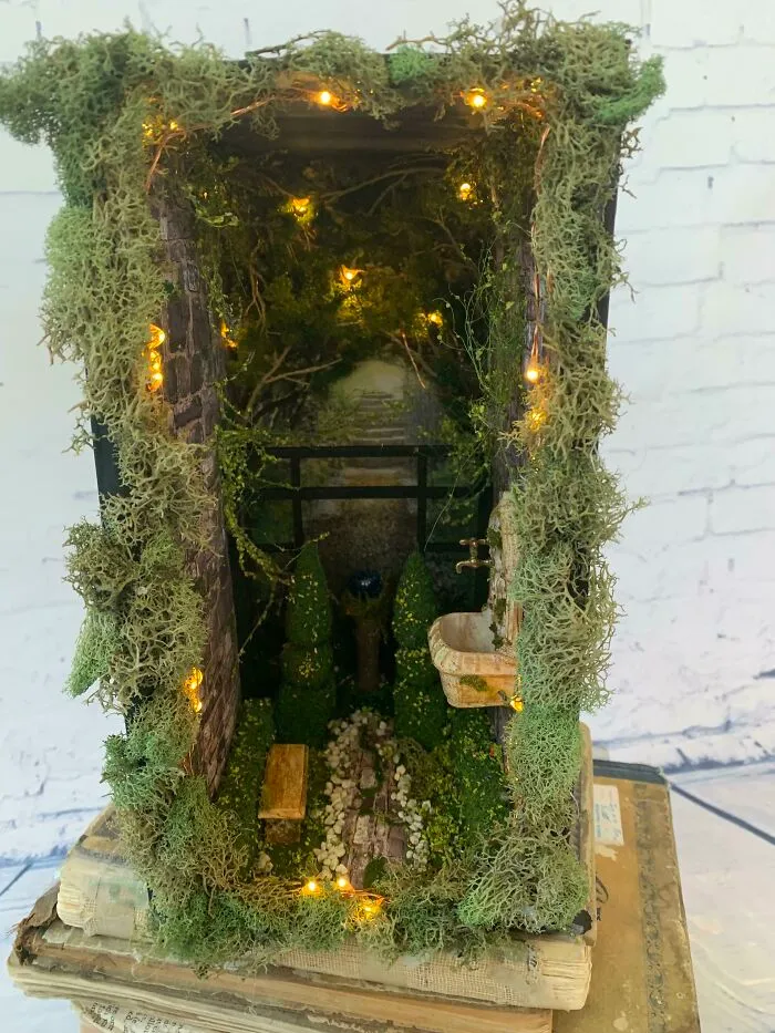 A moss covered secret garden book nook with lights and miniature plants