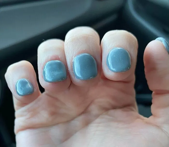 Close-up of thick grey nail polish on uneven nails showing beauty procedures fails.