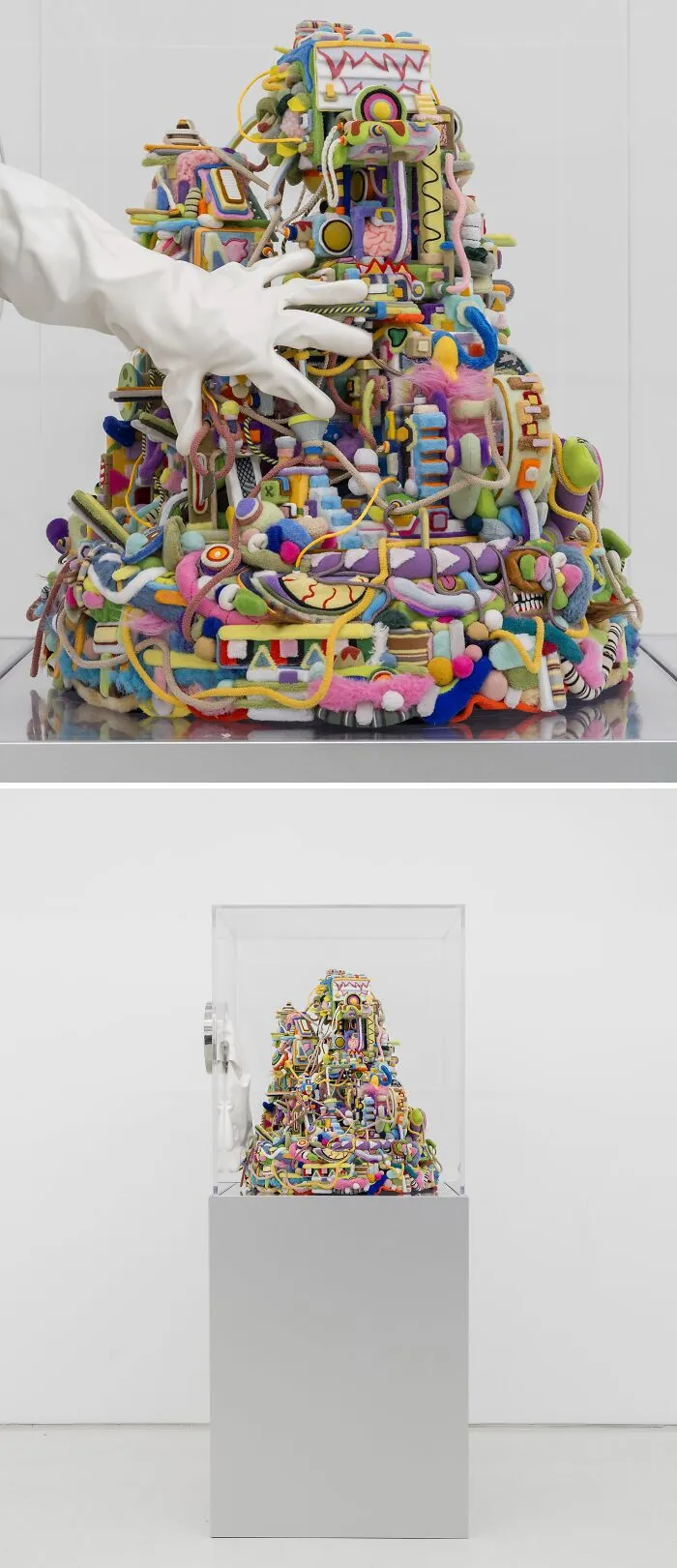 A hand wearing a white glove touching a colorful, chaotic, textured mound of unusual sculptures