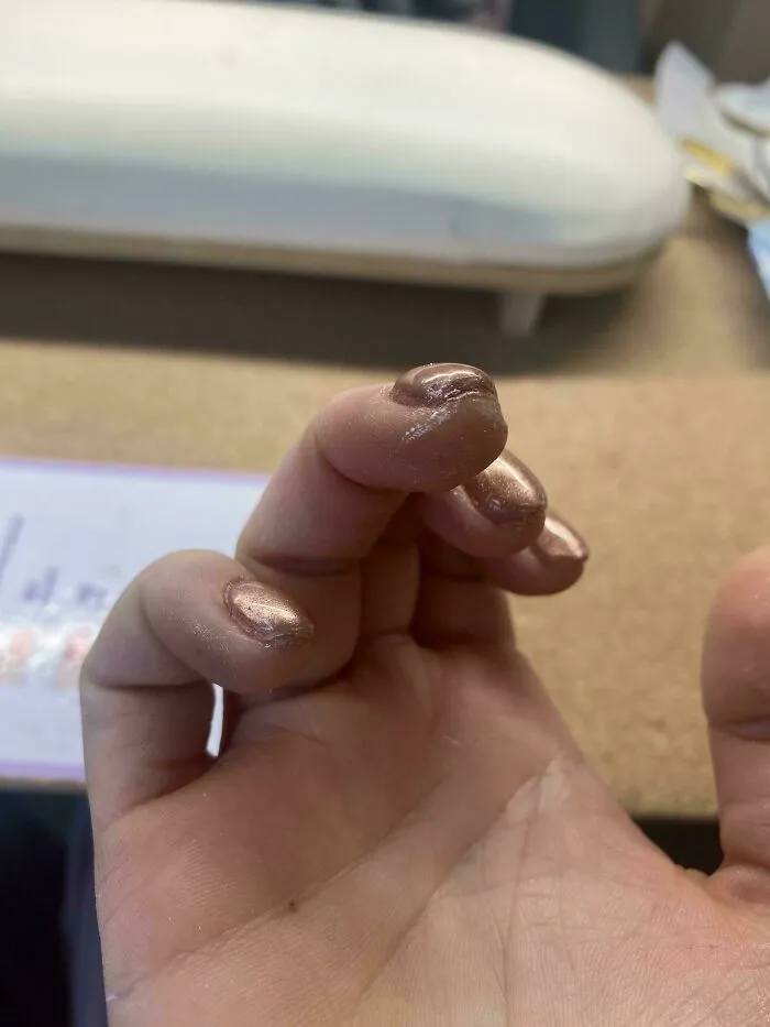 A close-up of a hand with messy, poorly applied metallic nail polish, indicating common beauty procedures fails.