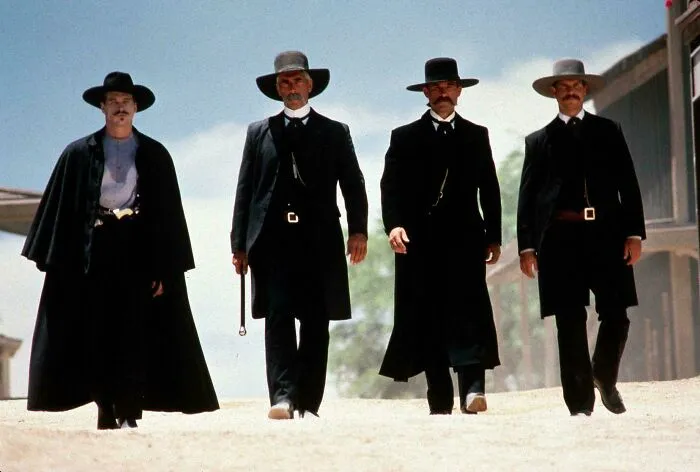Four cowboys from the '90s movie Tombstone walking side by side on a dirt road
