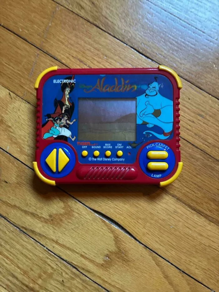An old Tiger Electronics Aladdin handheld game on a wooden floor, a symbol of the 90s.