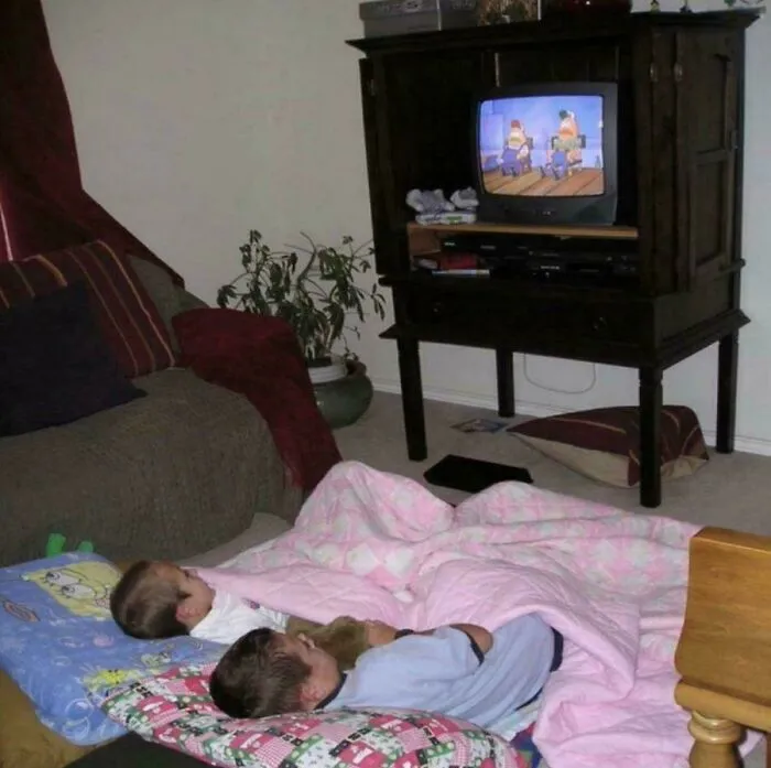 Two kids lying on the floor watching cartoons on a CRT television, reminiscing about the 90s.